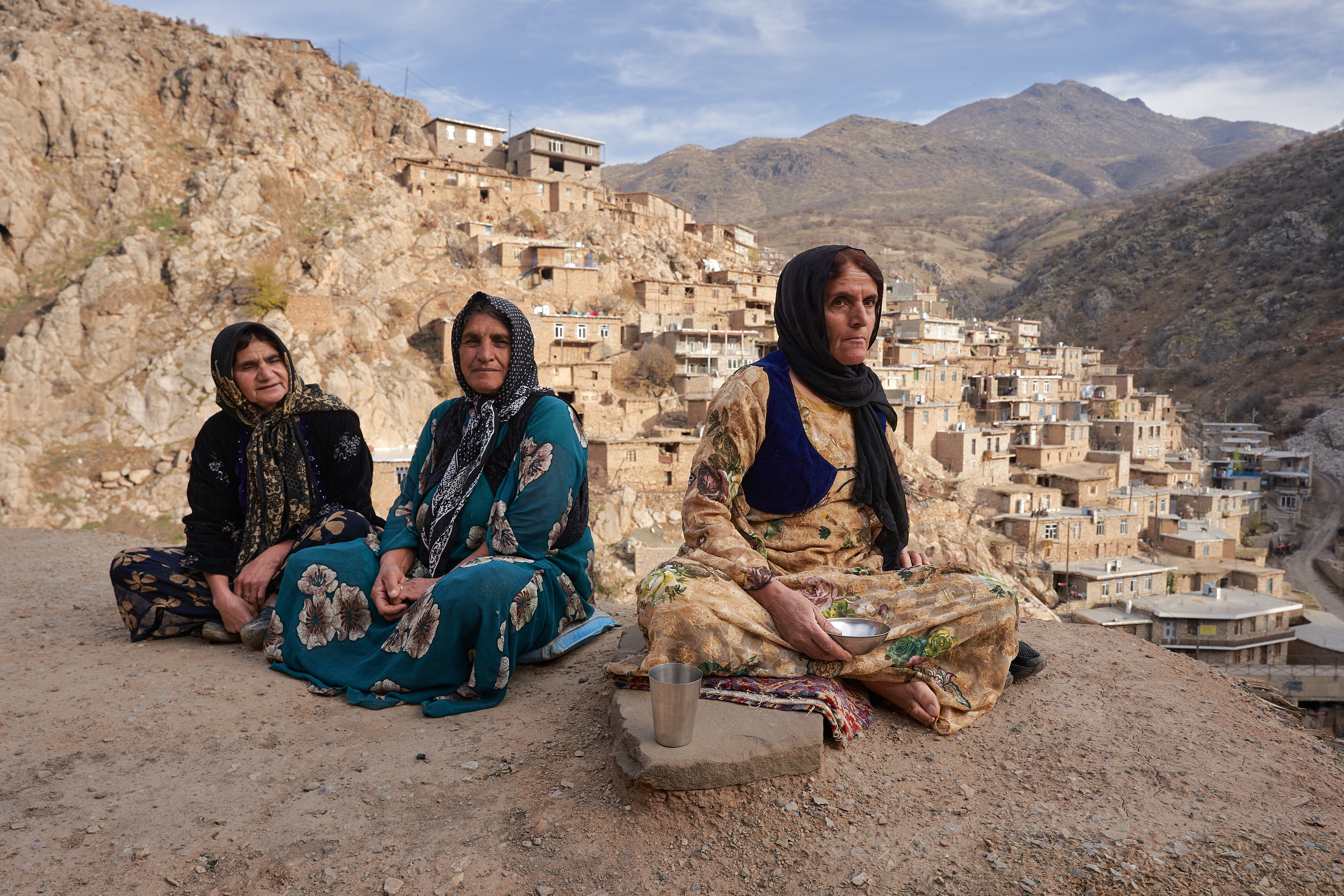 Three middle-aged Kurdish women sitting on the house's earthy roof overlooking the mountain village